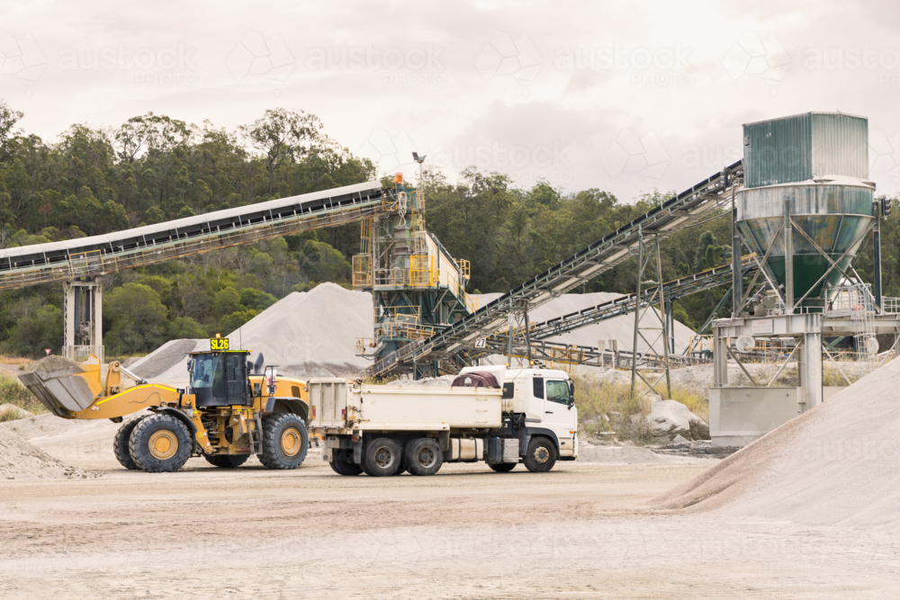 Loader and tipper truck at a quarry site with machinery in background - Australian Stock Image