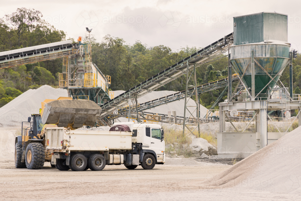 Loader and tipper truck at a quarry site with machinery in background - Australian Stock Image