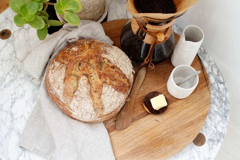 Loaf of bread, butter and filter coffee on wooden board and marble table - Australian Stock Image