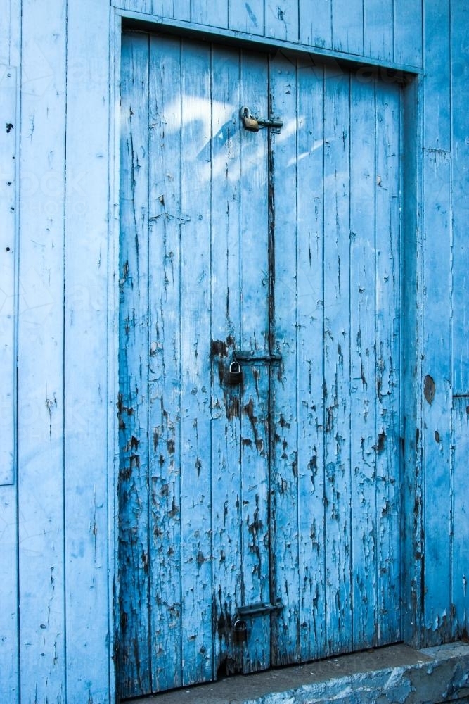 Locked and bolted old blue wooden door with paint peeling off - Australian Stock Image