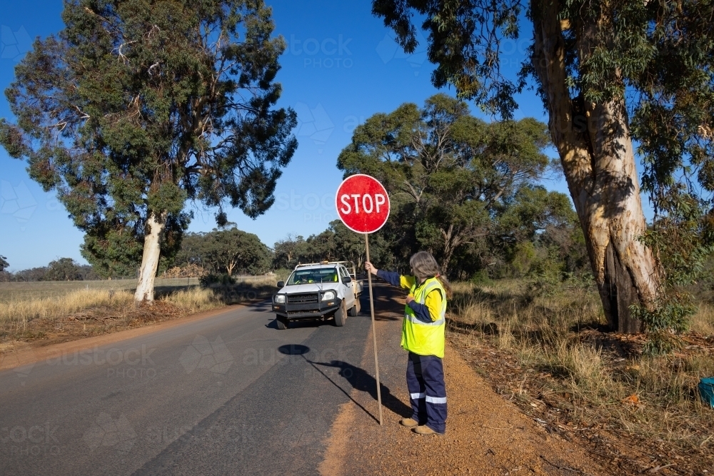 lollipop stop sign being held by worker wearing hi vis vest on side of road - Australian Stock Image