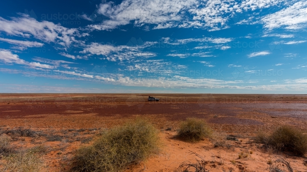Lone 4WD travelling across flat red outback - Australian Stock Image
