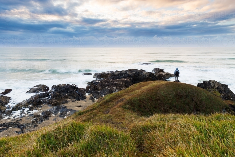 Lone figure standing on a headland overlooking the ocean - Australian Stock Image