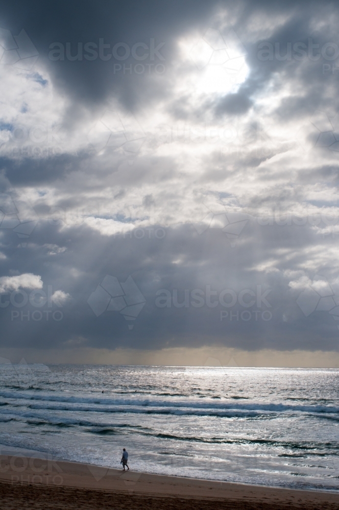 Lone person walking along beach with a dramatic sky above - Australian Stock Image