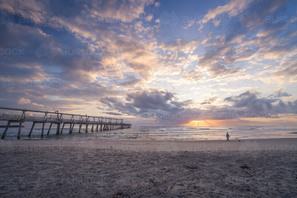 Lone person walking on beach at sunrise - Australian Stock Image