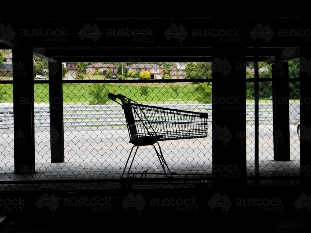 Lone shopping trolley in dark supermarket parking area - Australian Stock Image