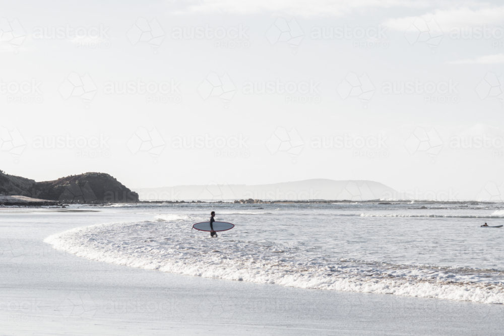 Lone surfer entering water in morning light - Australian Stock Image
