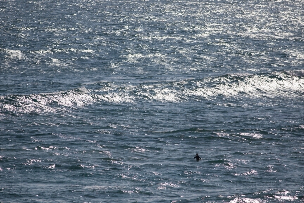 Lone surfer sitting on board waiting for a wave - Australian Stock Image