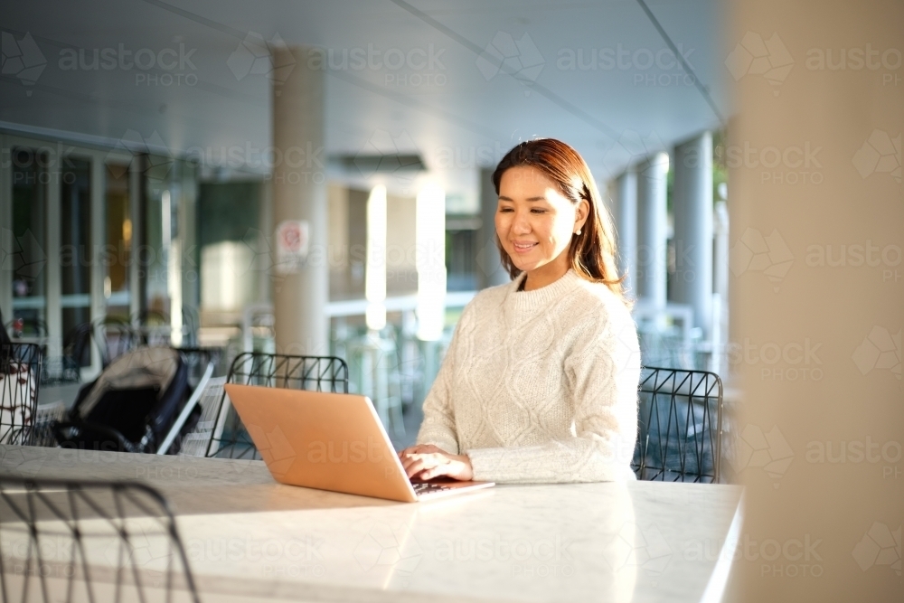 Lone woman working on laptop in seated area - Australian Stock Image