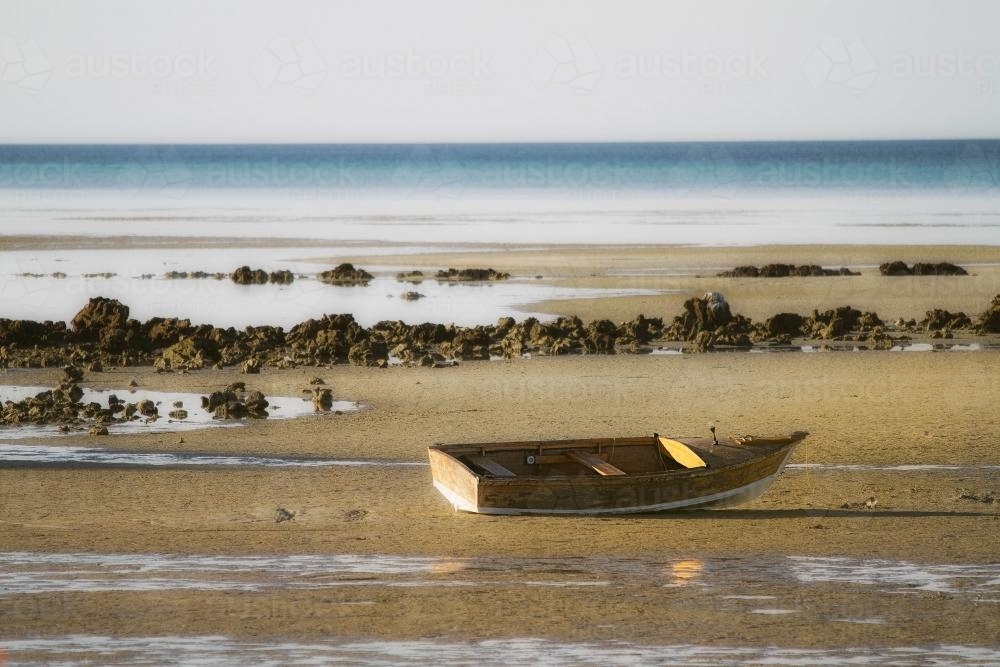 Lone wooden boat sitting on sand at low tide - Australian Stock Image