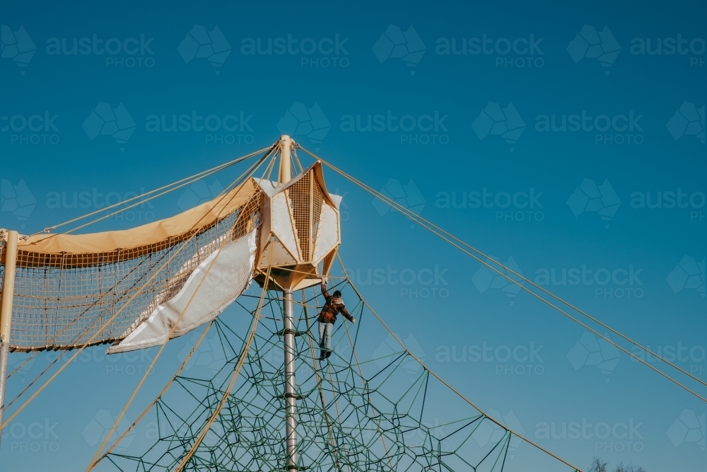 Lone young child hanging from rope playground against clear sky - Australian Stock Image