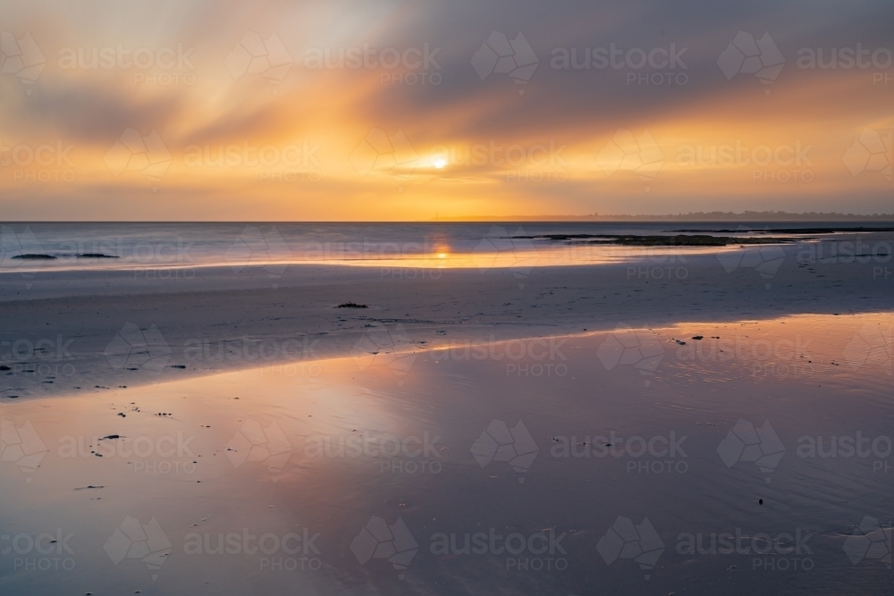 Long exposure of a hazy sunset over a sandy beach and reflections in a large pool of water - Australian Stock Image