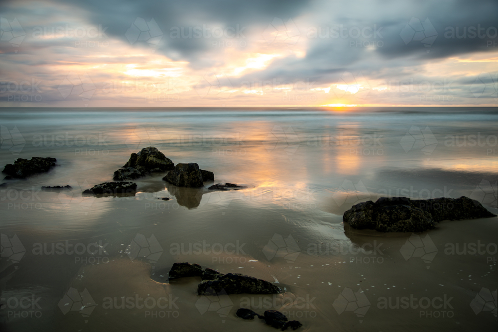 Long exposure of ocean and boulders on beach at dawn. - Australian Stock Image