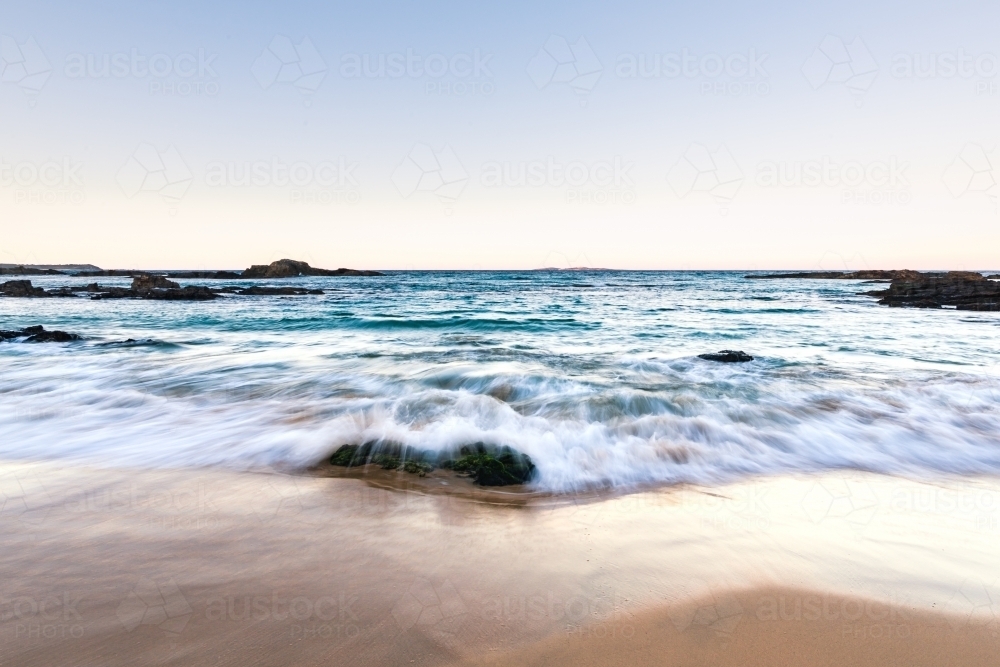 Long exposure of water flowing over rocks at the beach  in the late afternoon light - Australian Stock Image