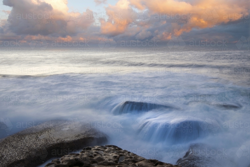 long exposure of waves over rocks at sunrise - Australian Stock Image