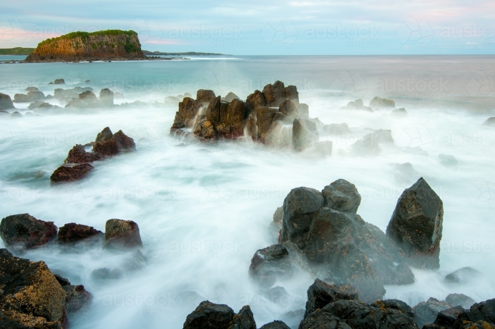 Long exposure of waves over sharp rocks with an island in the background - Australian Stock Image