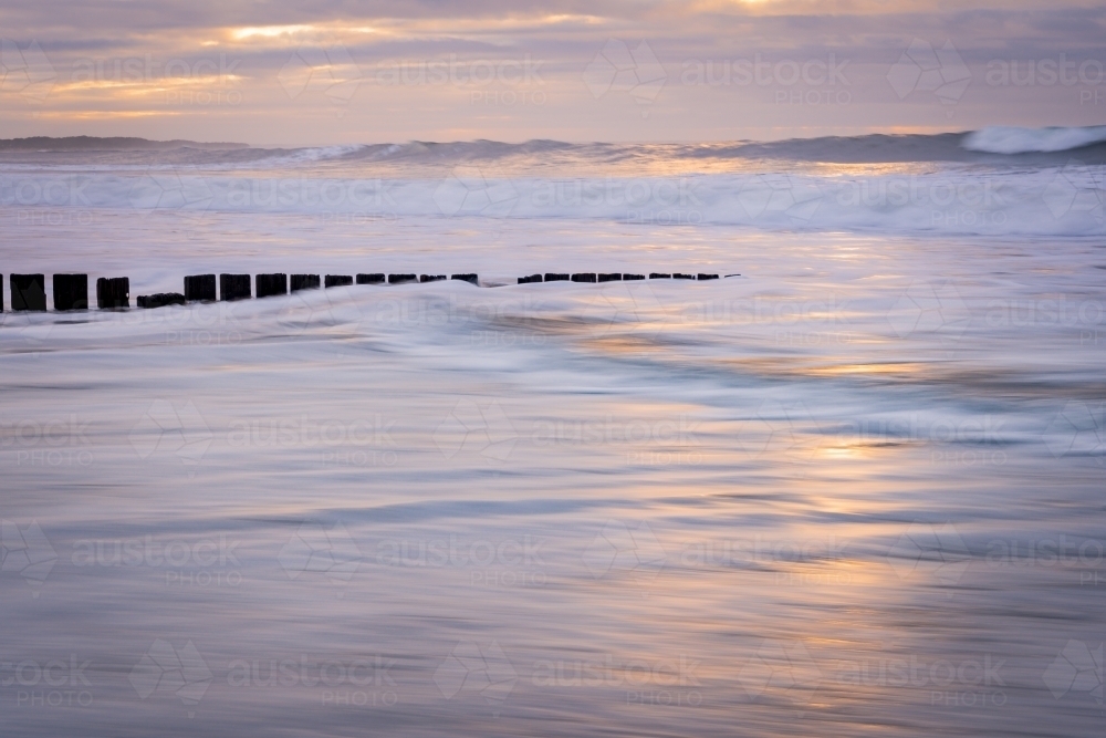 Long exposure of waves rushing along a beach at sunrise - Australian Stock Image