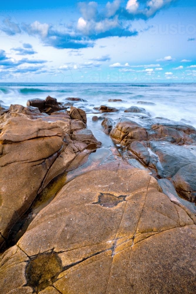 Long exposure sunset shot of waves washing over seaside rocks - Australian Stock Image