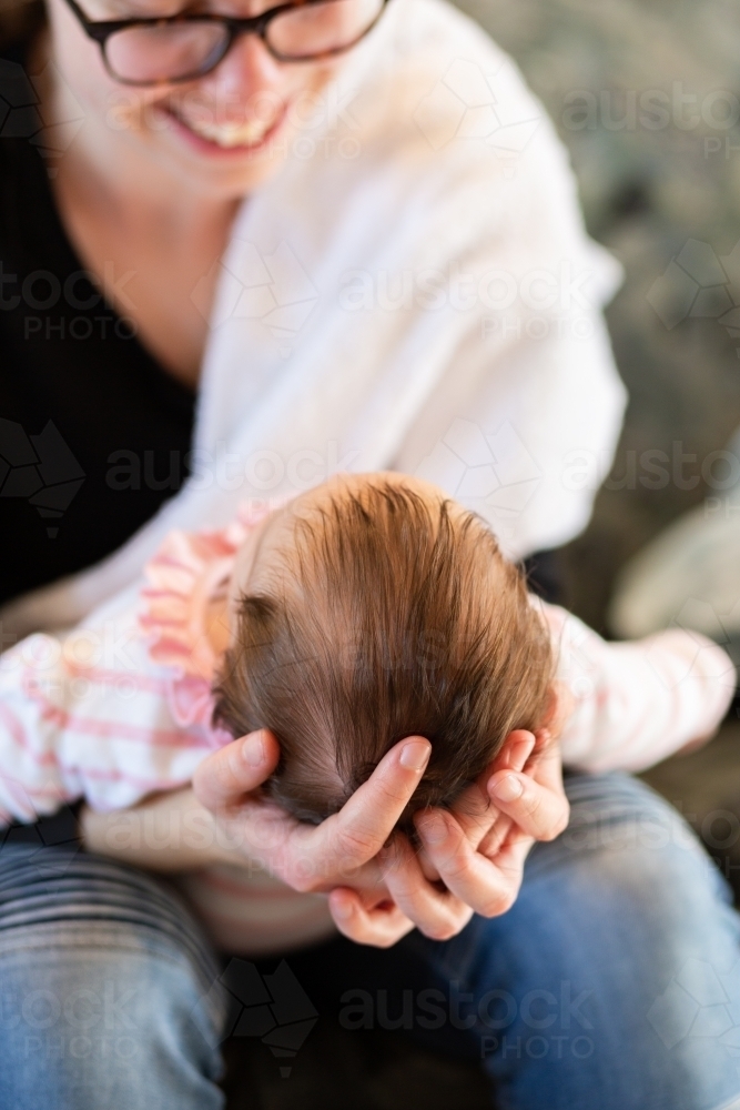 long hair on head of baby girl being held by her young aunty smiling together inside home - Australian Stock Image