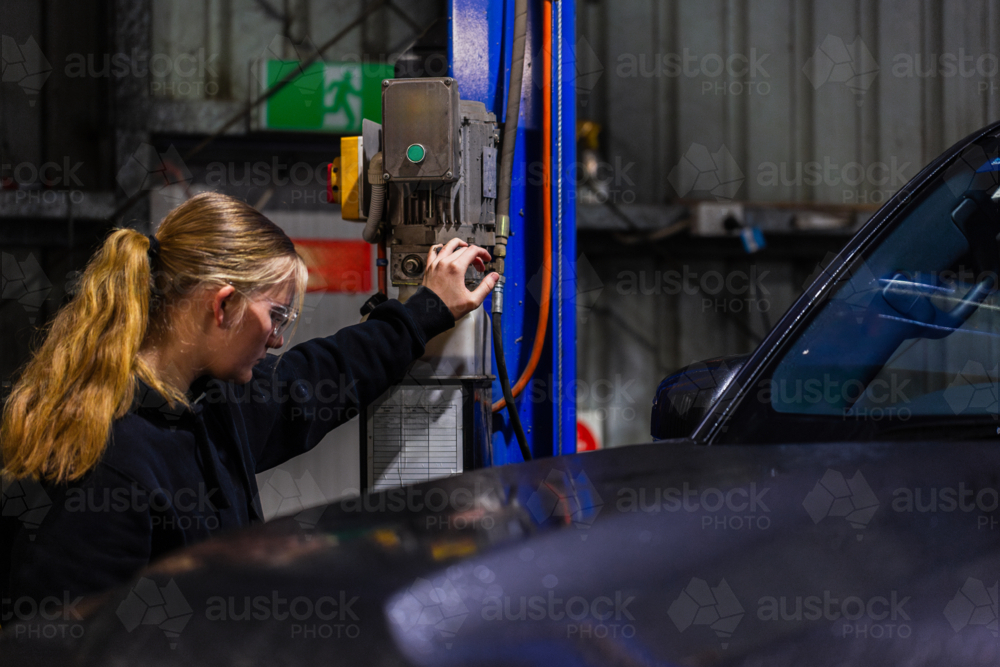 Long-haired mechanic operating a control panel of blue hydraulic lift system - Australian Stock Image