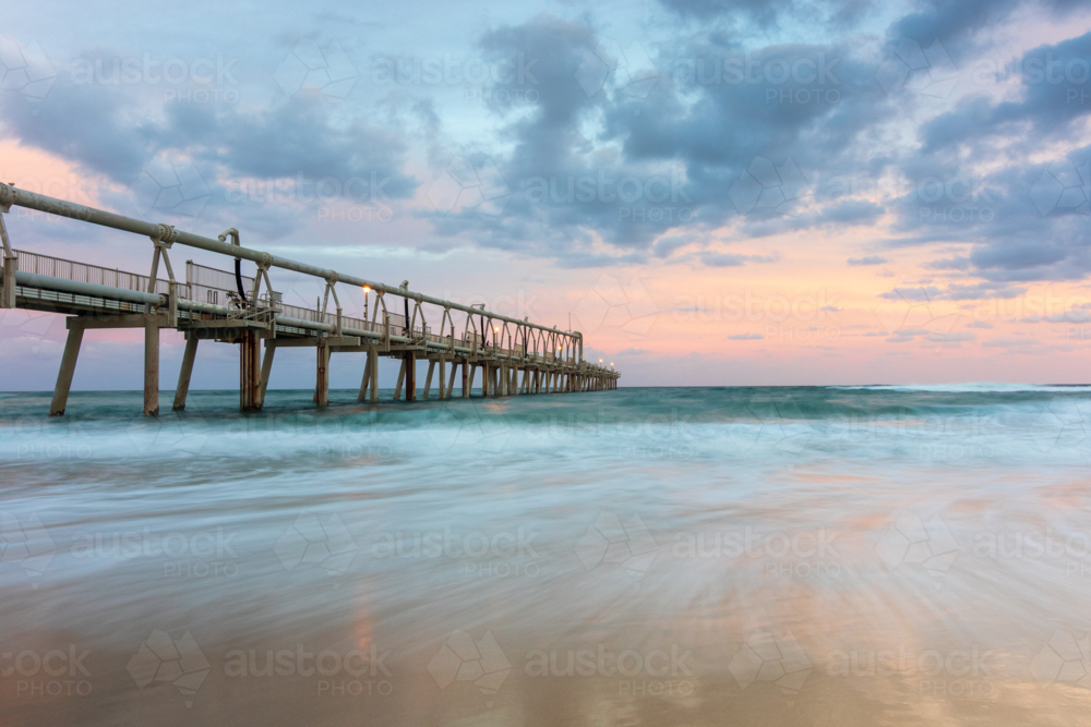 Long jetty stretching into the ocean with a pastel, cloudy sky - Australian Stock Image