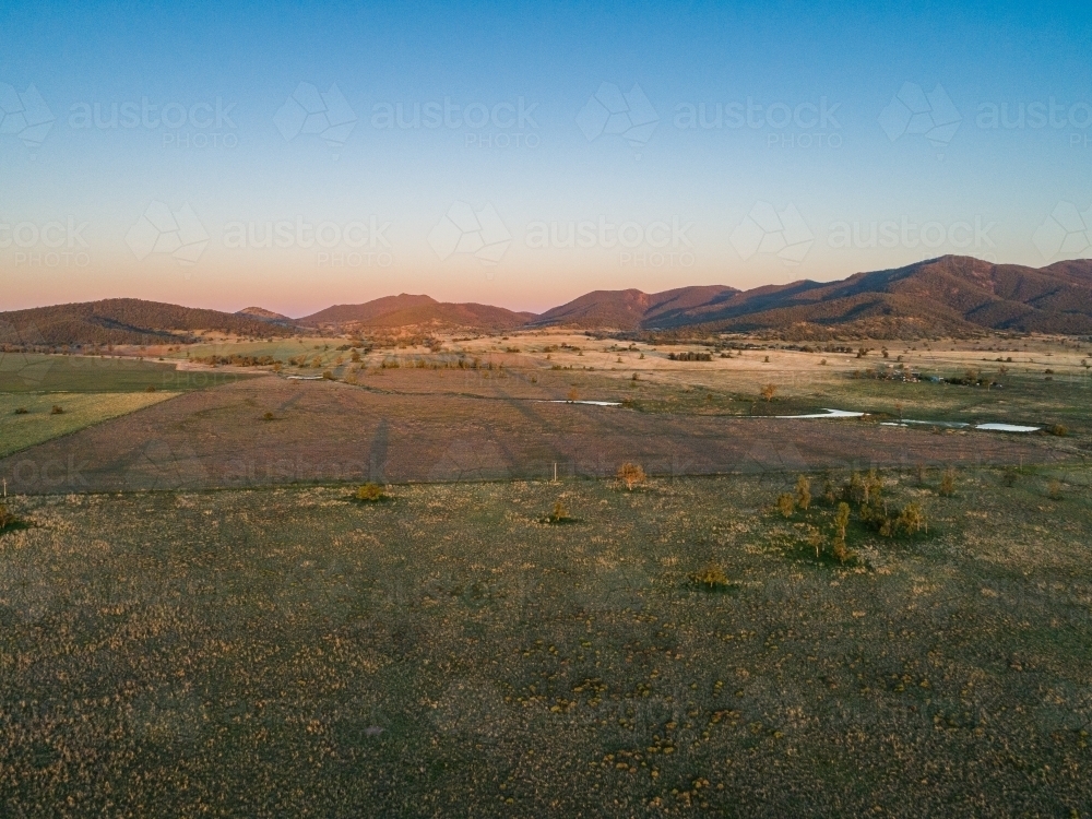 Long shadowed landscape and dusk light on distant hills over pastoral land - Australian Stock Image