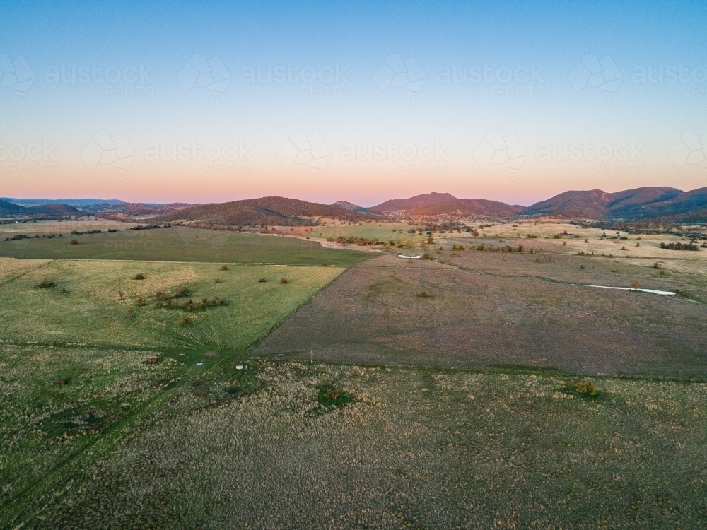 Long shadowed landscape and dusk light on distant hills over pastoral land - Australian Stock Image