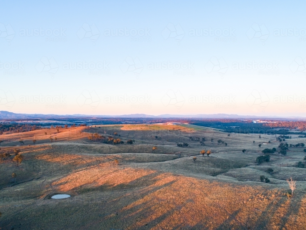 Long shadows on hills in paddock with small dam - Australian Stock Image