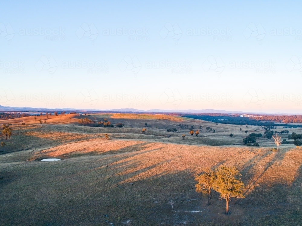 Long shadows on hills in paddock with small dam - Australian Stock Image
