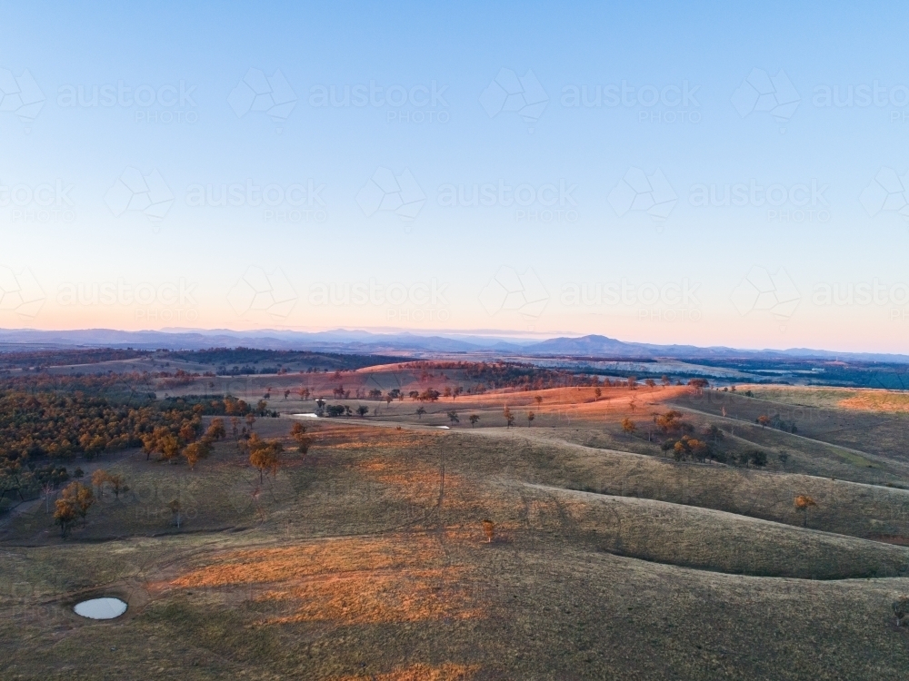 Long shadows on hills in paddock with small dam - Australian Stock Image