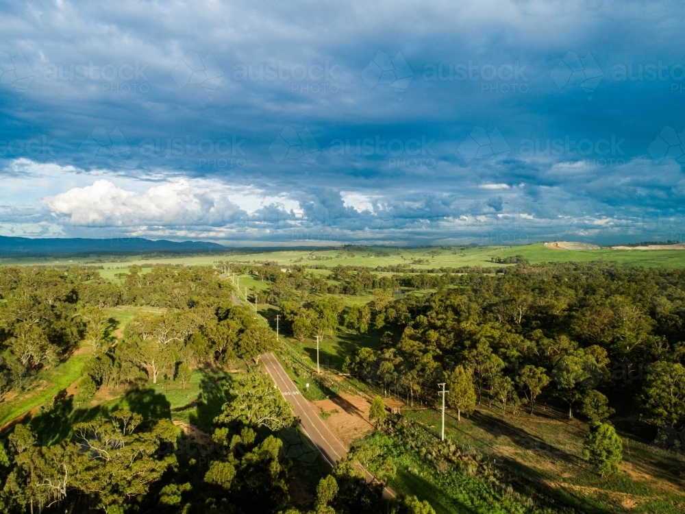 Long shadows over paddock with green grass and rain clouds - Australian Stock Image