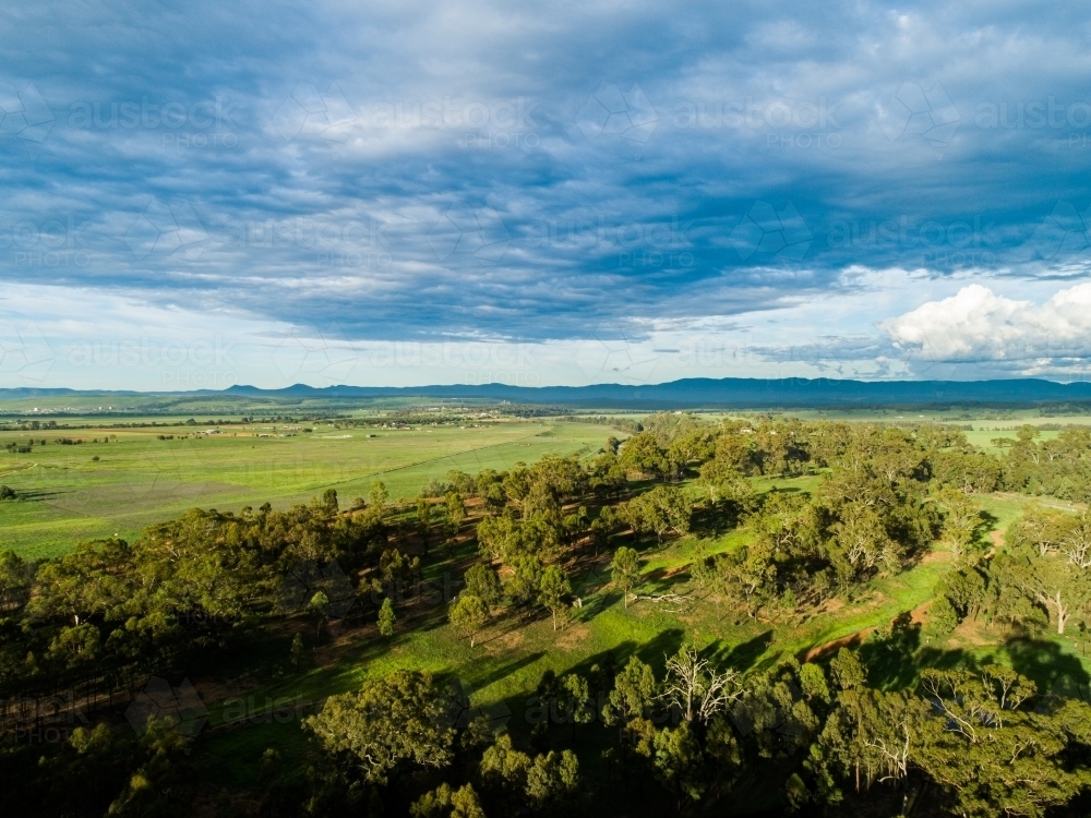Long shadows over paddock with green grass and rain clouds - Australian Stock Image