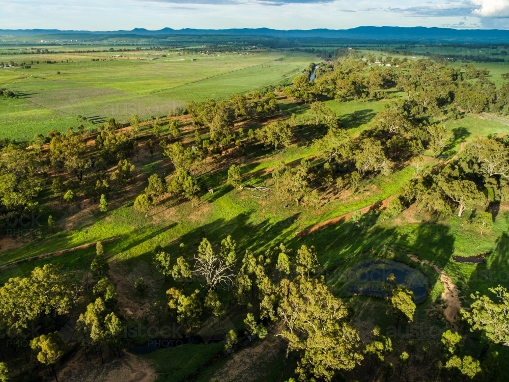 Long shadows over paddock with green grass and rain clouds - Australian Stock Image