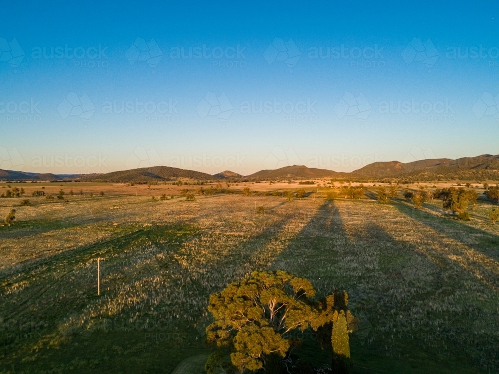 Long shadows stretch towards hills at sunset looking away from sun over farmland - Australian Stock Image