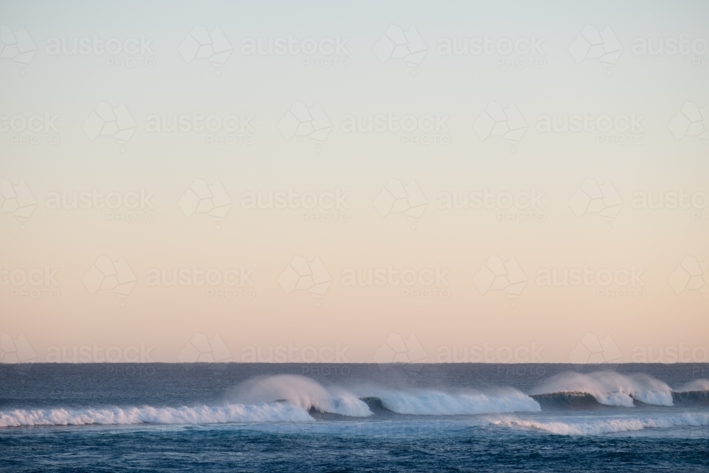 Long shot of breaking waves with spray and pastel sky - Australian Stock Image