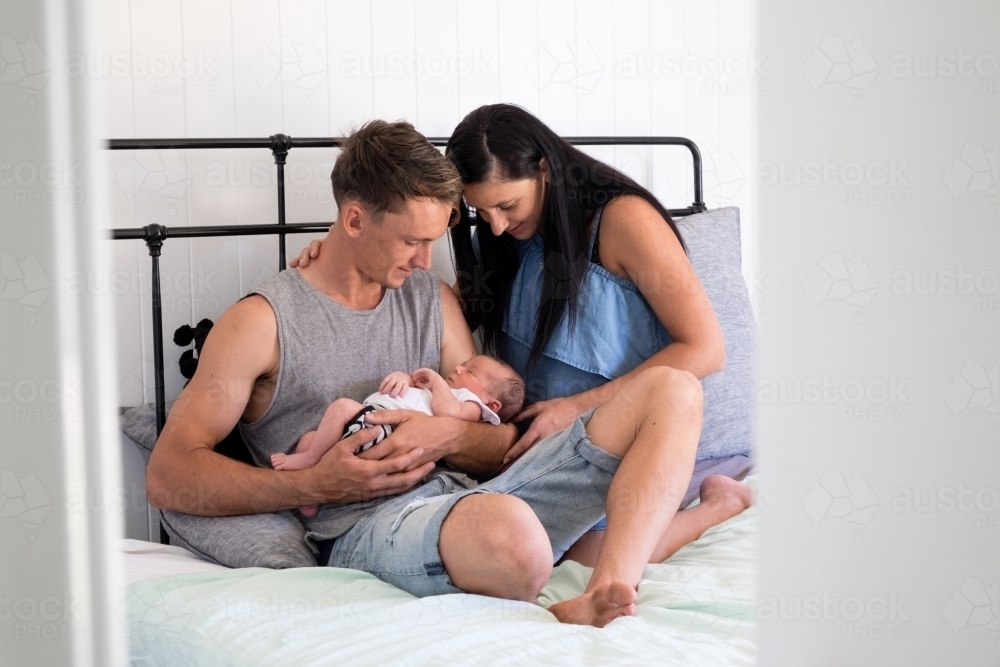 long shot of mother and father holding newborn on bed in bedroom - Australian Stock Image