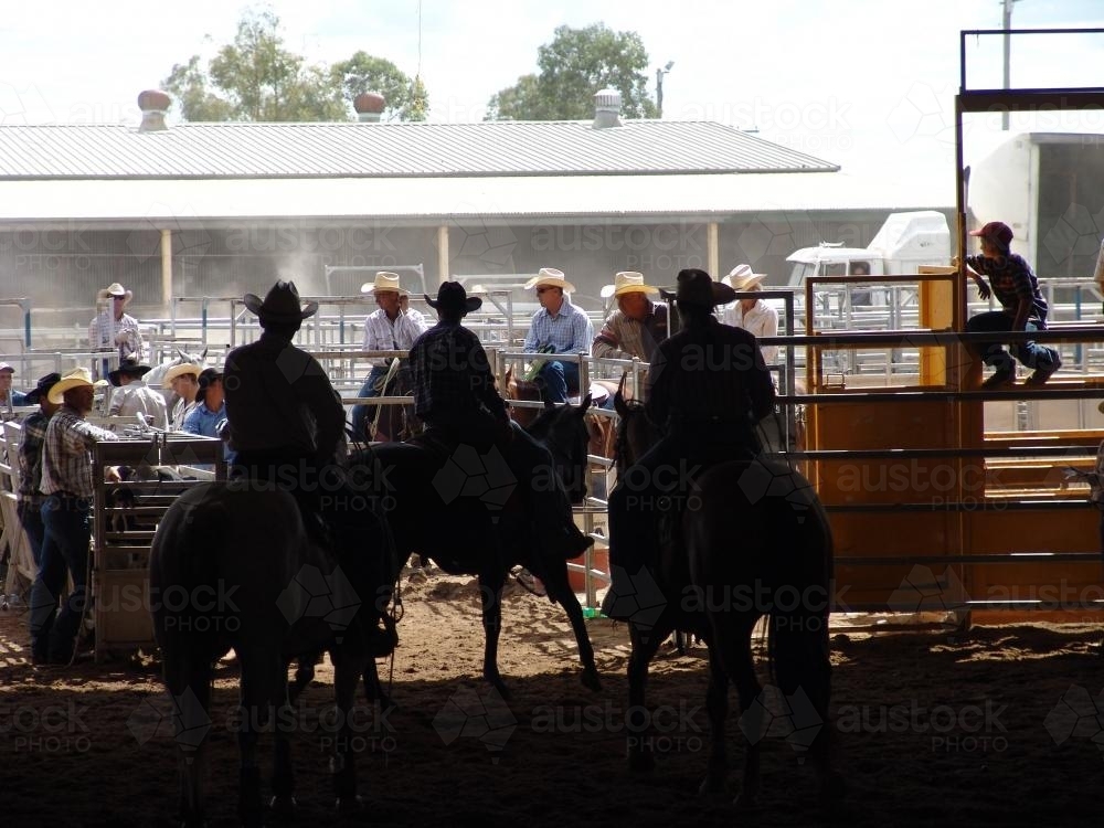 Long shot of rodeo with three riders silhouetted in foreground - Australian Stock Image