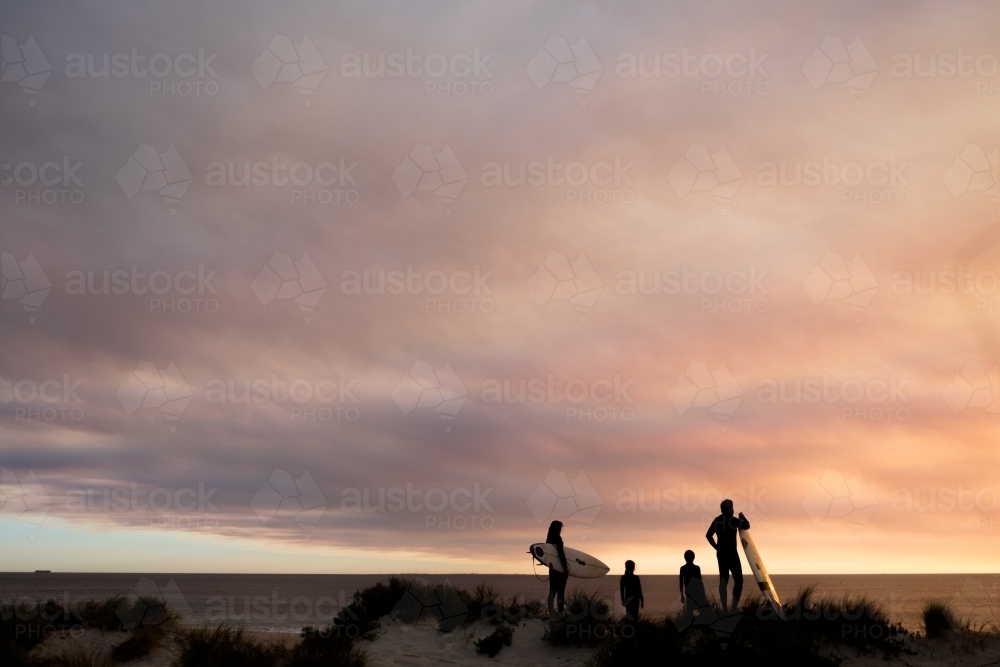 Long shot silhouette of family of four overlooking coastal seascape with moody sunset - Australian Stock Image