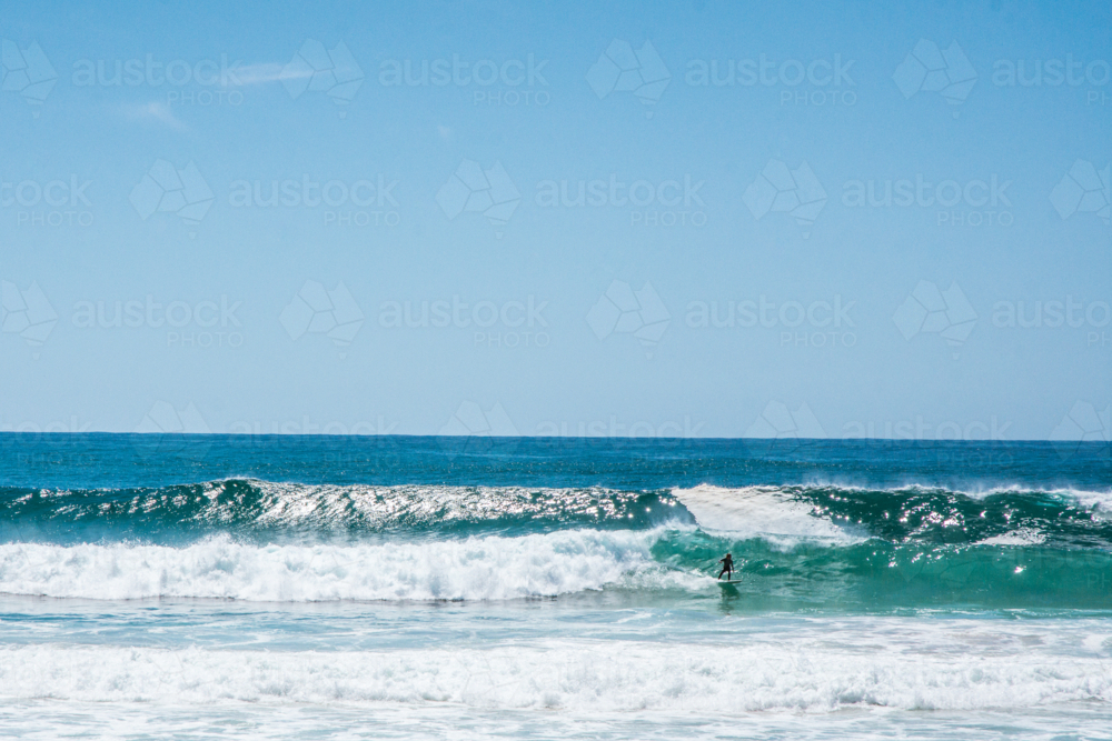 Long surfer on large waves with blue sky - Australian Stock Image