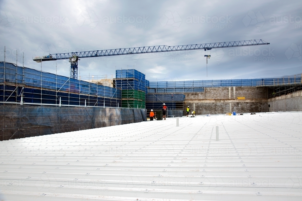 Looking across a metal roof at construction workers on an industrial building site - Australian Stock Image