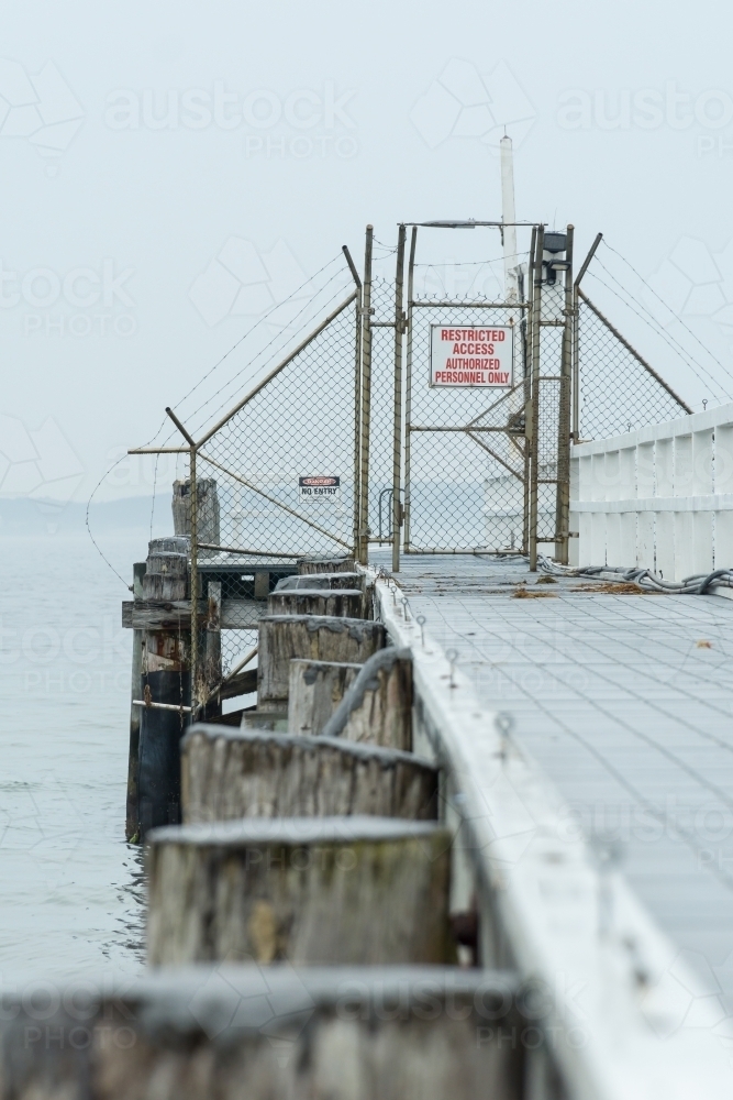 Looking along a seaside jetty to a locked gate and exclusion fencing - Australian Stock Image