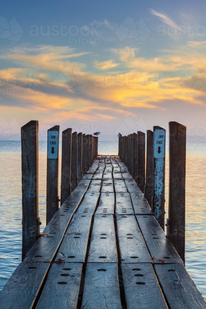 Looking along a wet wooden jetty toward a dawn sky. - Australian Stock Image