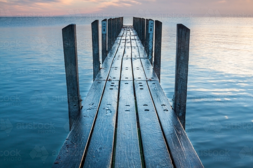 Looking along a wet wooden jetty toward a dawn sky. - Australian Stock Image