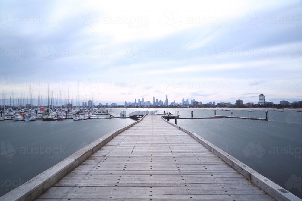 Looking along jetty to moored boats and city in distance - Australian Stock Image