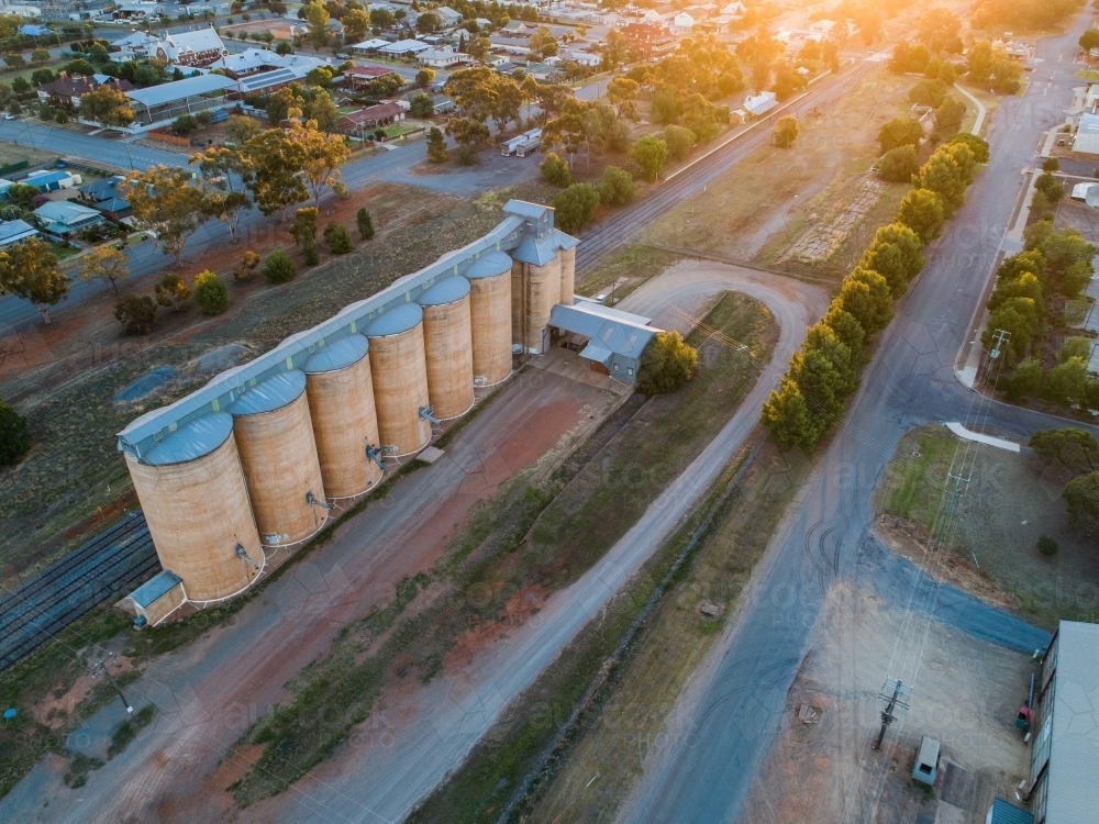 Looking along the tops of a line of grain silos beside a railway line at sunset - Australian Stock Image