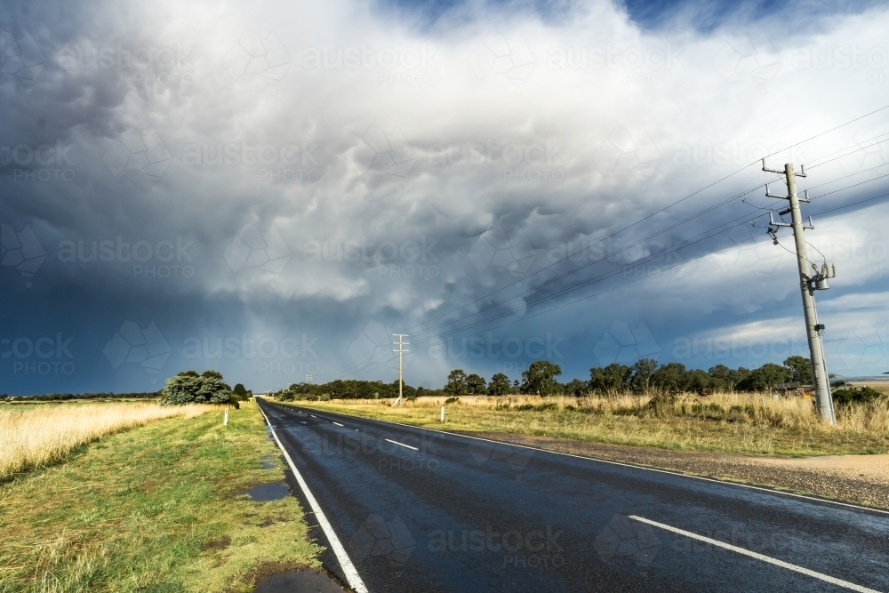 Looking down a country road towards a large thunderstorm - Australian Stock Image