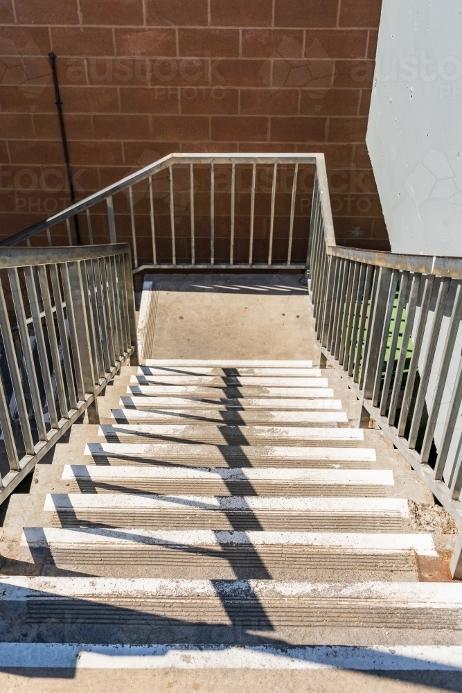 Looking down a stairwell with metal railings and shadows crossing the steps - Australian Stock Image