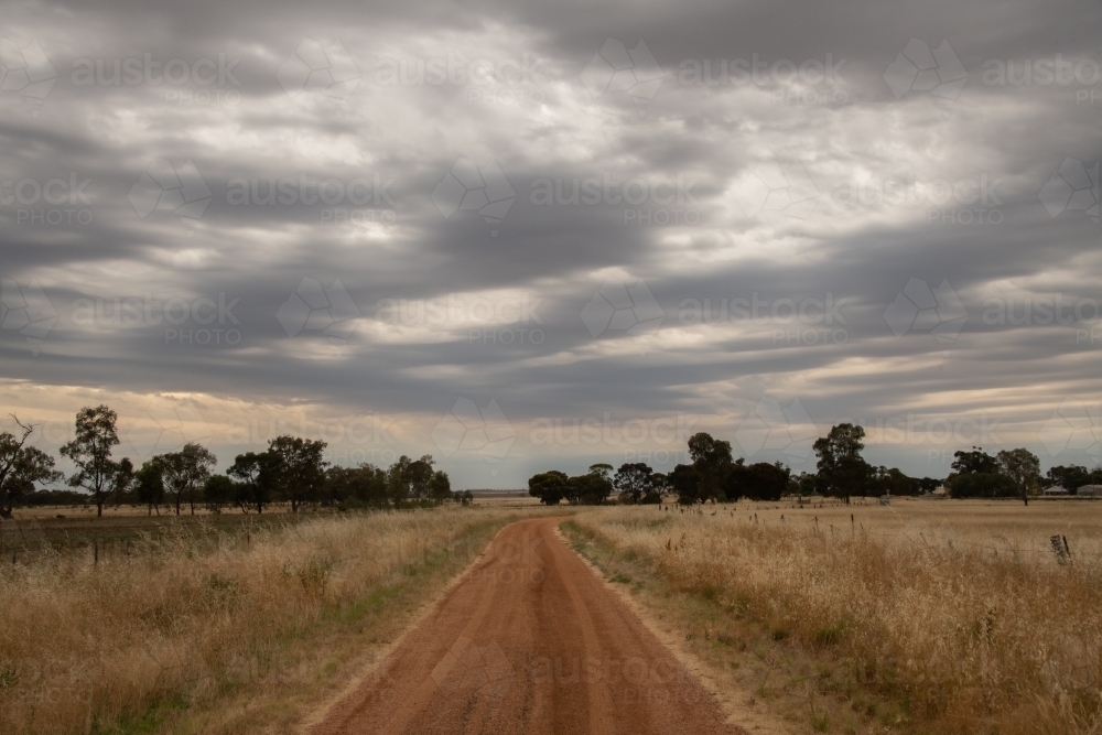 Looking down along the dirt road with the storm clouds approaching. - Australian Stock Image