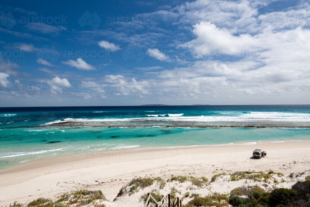 Looking down and out on a view of  man with 4wd vehicle on an isolated beach with turquoise lagoon - Australian Stock Image