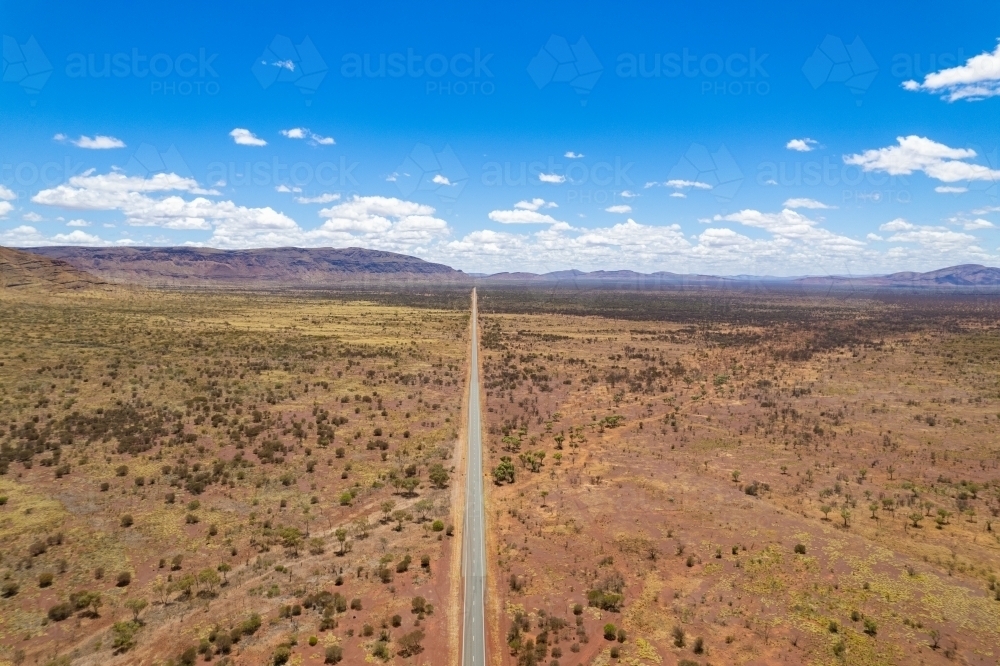 Looking down at a long straight asphalt road with the mountains in the distance - Australian Stock Image